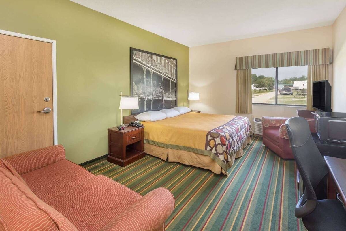 Een hotelkamer met een bed, een bureau met stoel, een televisie, een raam met uitzicht en een deur.