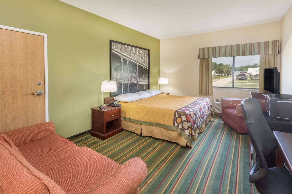 Hotelkamer met een bed, een bureau, een stoel, een televisie, een raam met gordijnen en een deur.