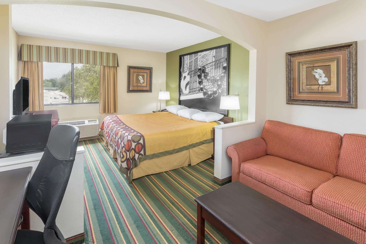 Een hotelkamer met een bed, een bureau met een computer, een rode bank en een groot raam met gordijnen.