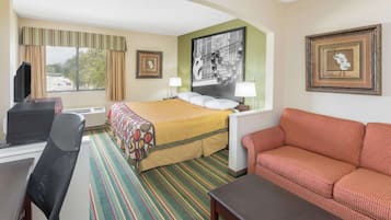 A hotel room with a bed, a desk with a computer, a red sofa, and a large window with curtains.