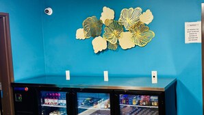 A vending machine area with three beverage dispensers, a blue wall, and a security camera. - Four Seasons Inn (Bottineau)