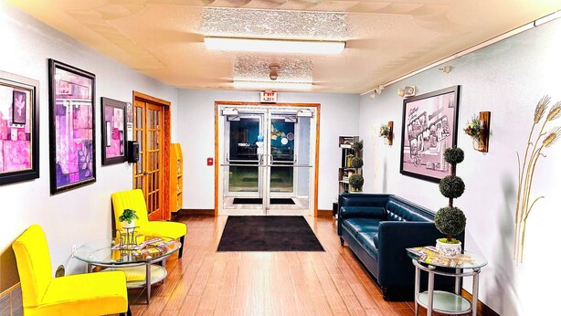 A hotel lobby with a reception desk, a blue sofa, yellow chairs, and framed artwork on the walls. - Four Seasons Inn (Bottineau)