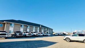 A large building with multiple parking spaces and a row of parked vehicles. - Four Seasons Inn (Bottineau)