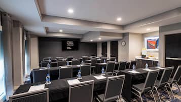 Un salón de conferencias con mesas, sillas y una pantalla mostrando 'FOUR POINTS BY SHEIKH'.