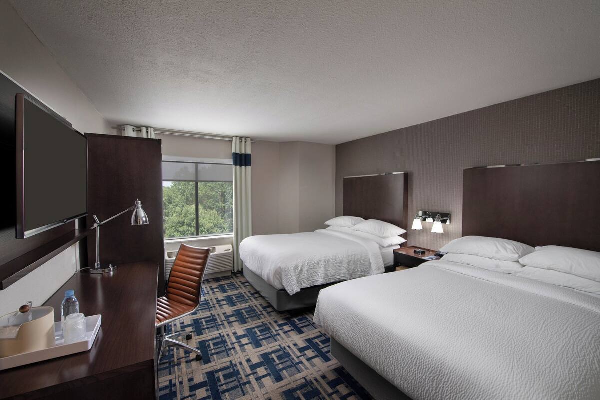 Een hotelkamer met twee bedden, een bureau met stoel, een televisie en een raam met gordijnen.