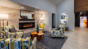 Un salon moderne avec des fauteuils à motifs, une table basse en bois placée au centre, une cheminée et un grand miroir mural.