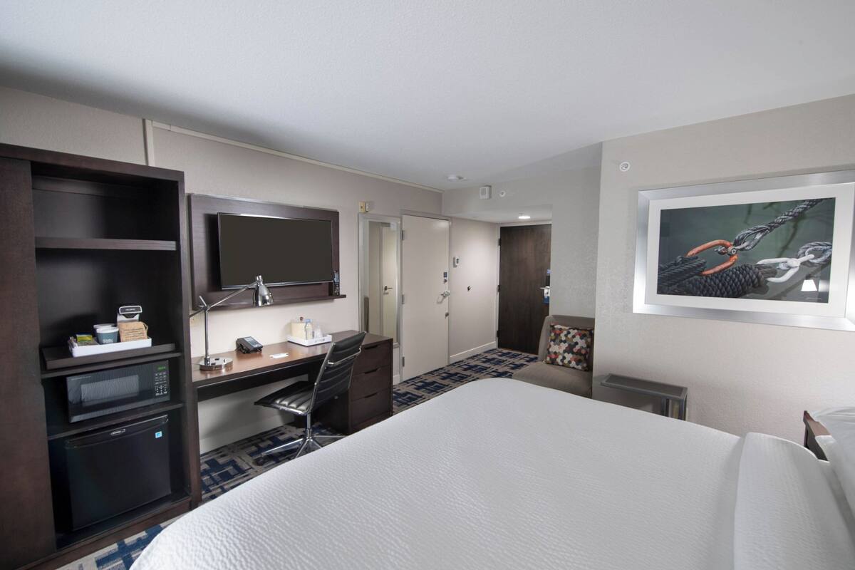Een hotelkamer met een bed, bureau, magnetron en een grote spiegel.
