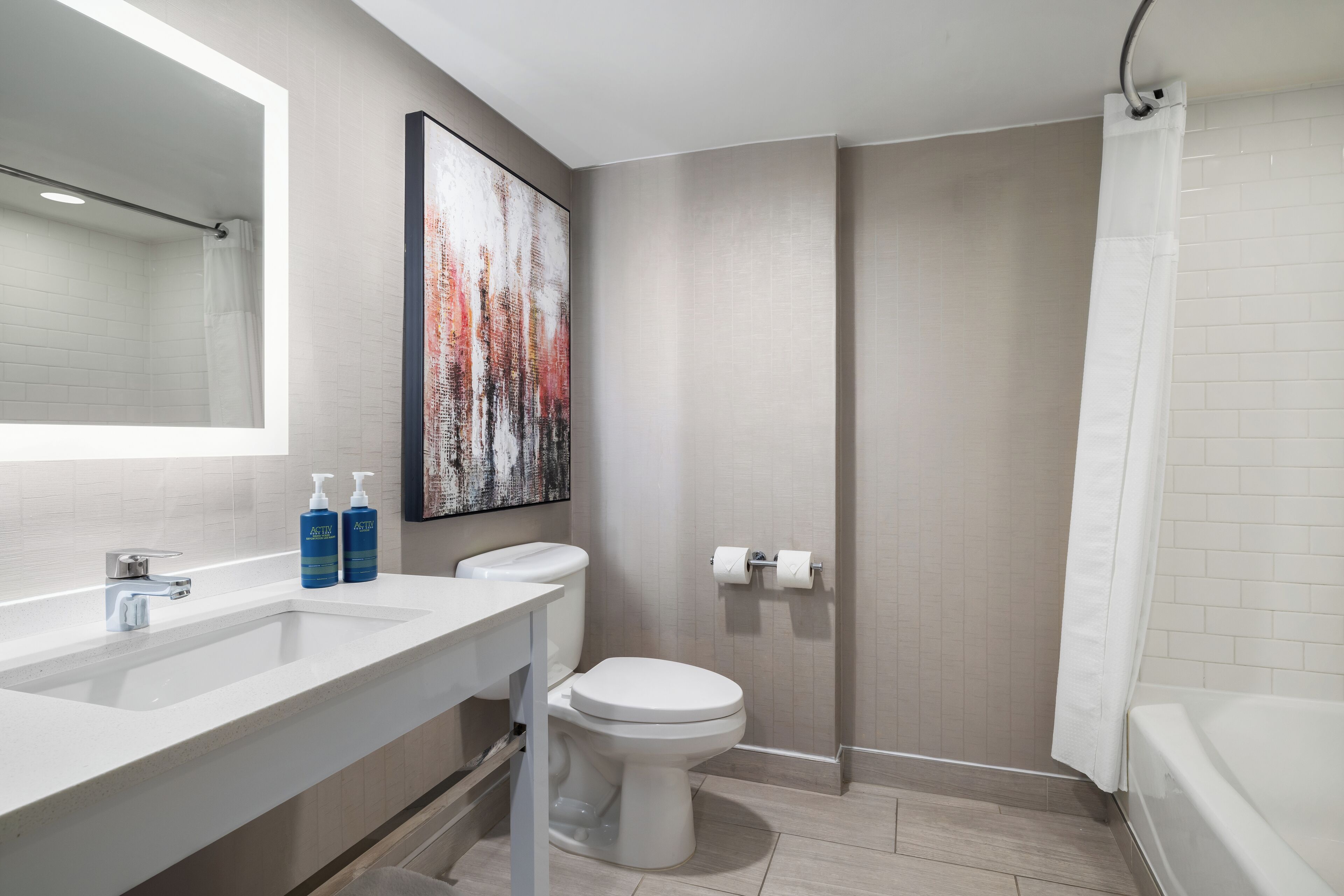 A modern bathroom with a white sink, a toilet, a shower with a curtain, and a large mirror.