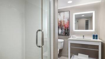Un baño moderno con cabina de ducha de vidrio, un lavabo blanco con espejo y un inodoro.