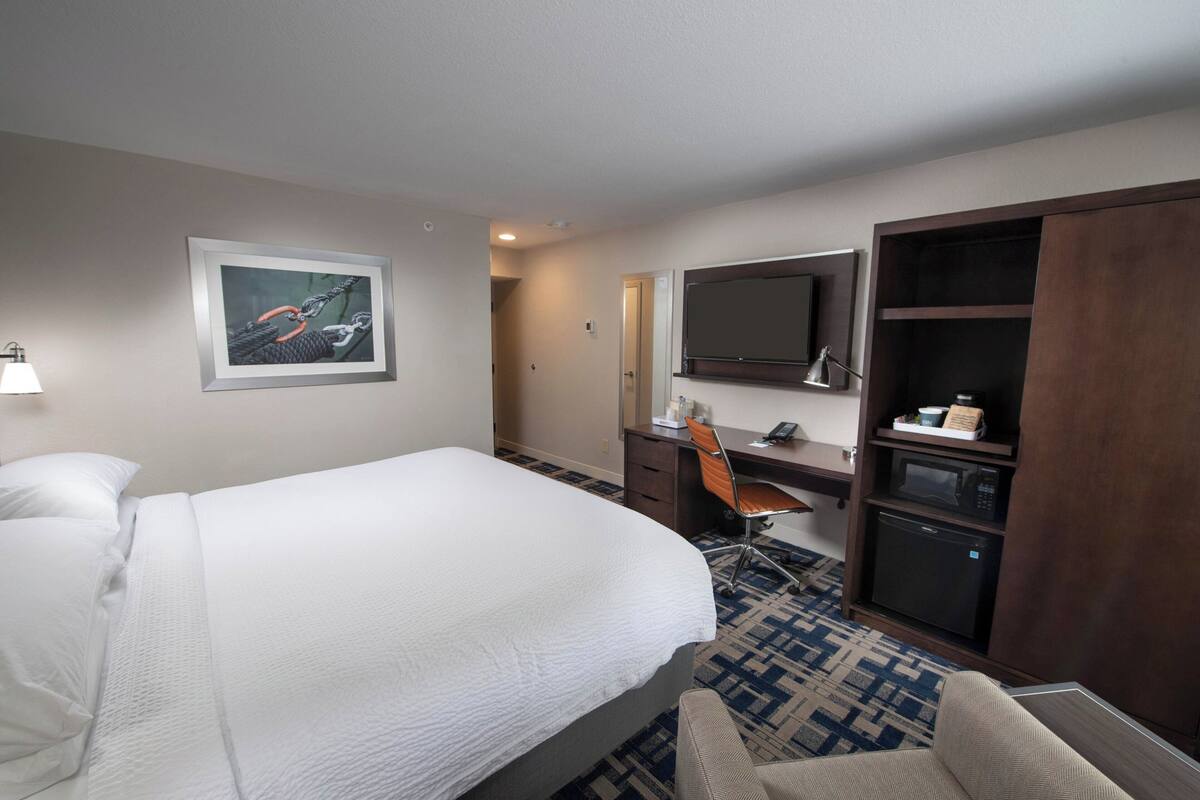 Een hotelkamer met een bed, een bureau, een stoel, een magnetron en een televisie.