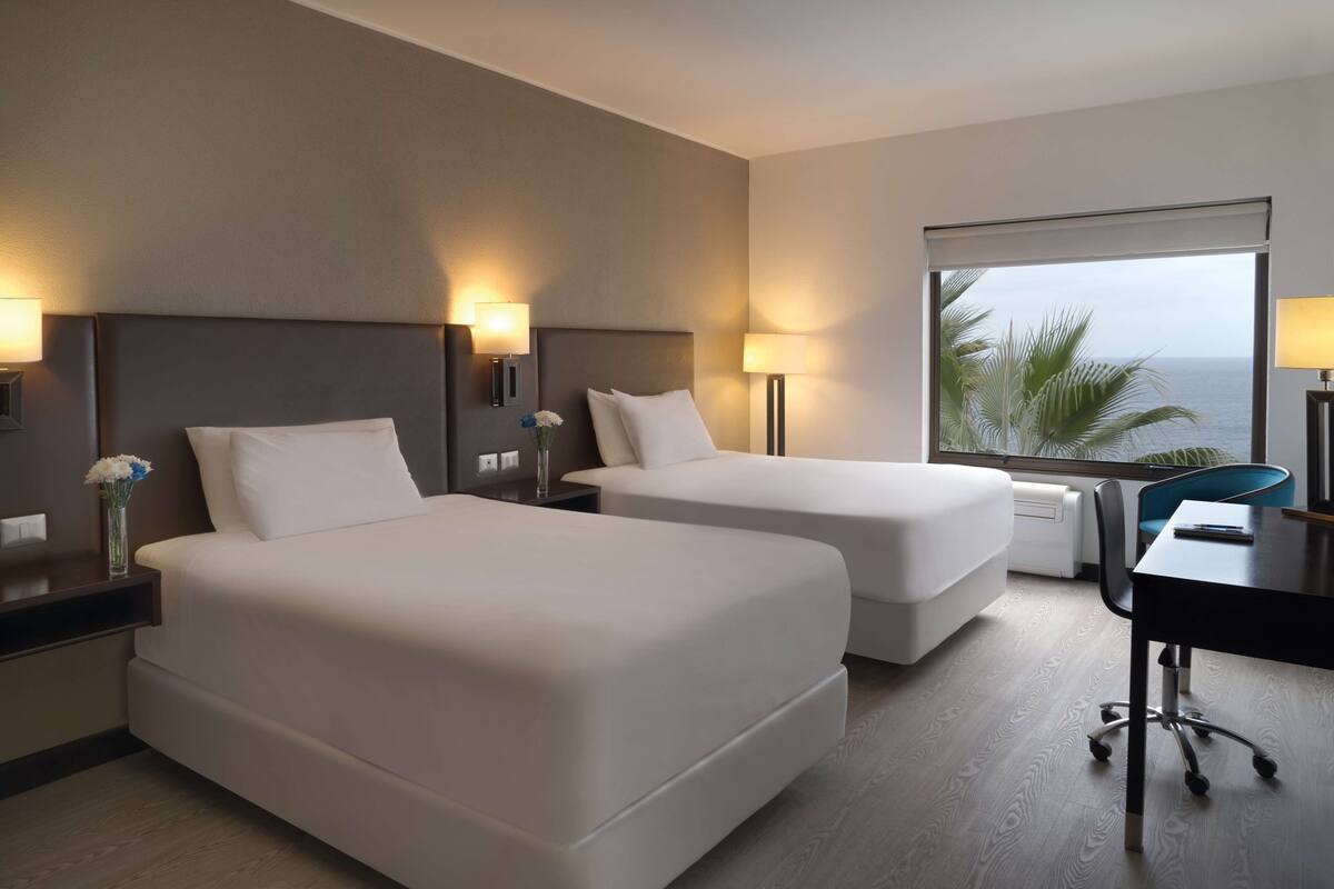 Habitación de hotel con dos camas, un escritorio y vista al océano.