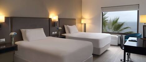 A hotel room with two beds, a desk, and a view of the ocean.