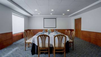 A conference room with a long table, chairs, a projector screen, and a carpeted floor.