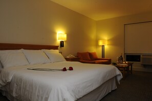 A hotel room with a large bed, two bedside lamps, a small table with a phone and a bottle, a chair, and a projector screen. - NH Antofagasta (Antofagasta)
