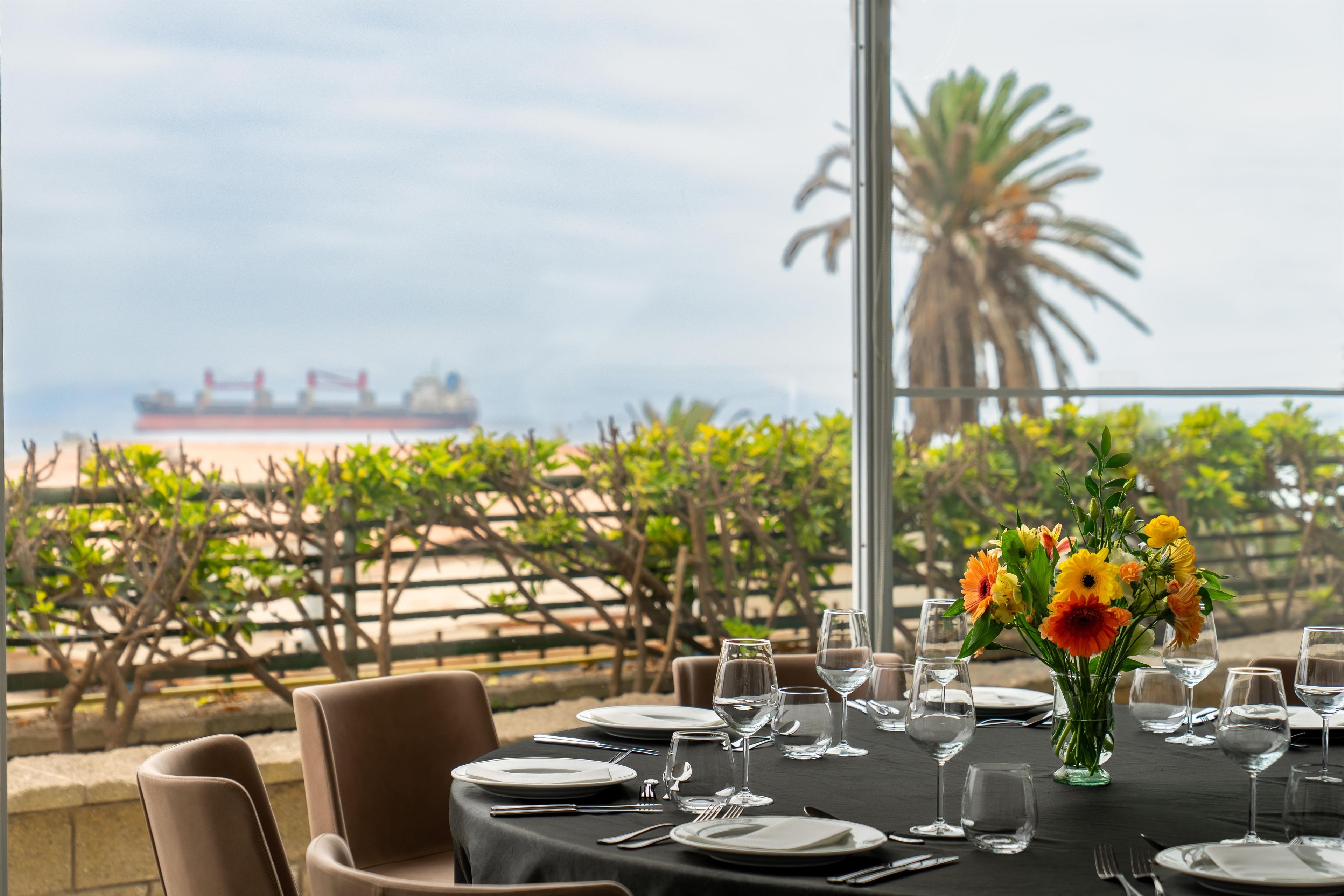 Mesa lista para comer con vista al océano y un barco en la distancia.