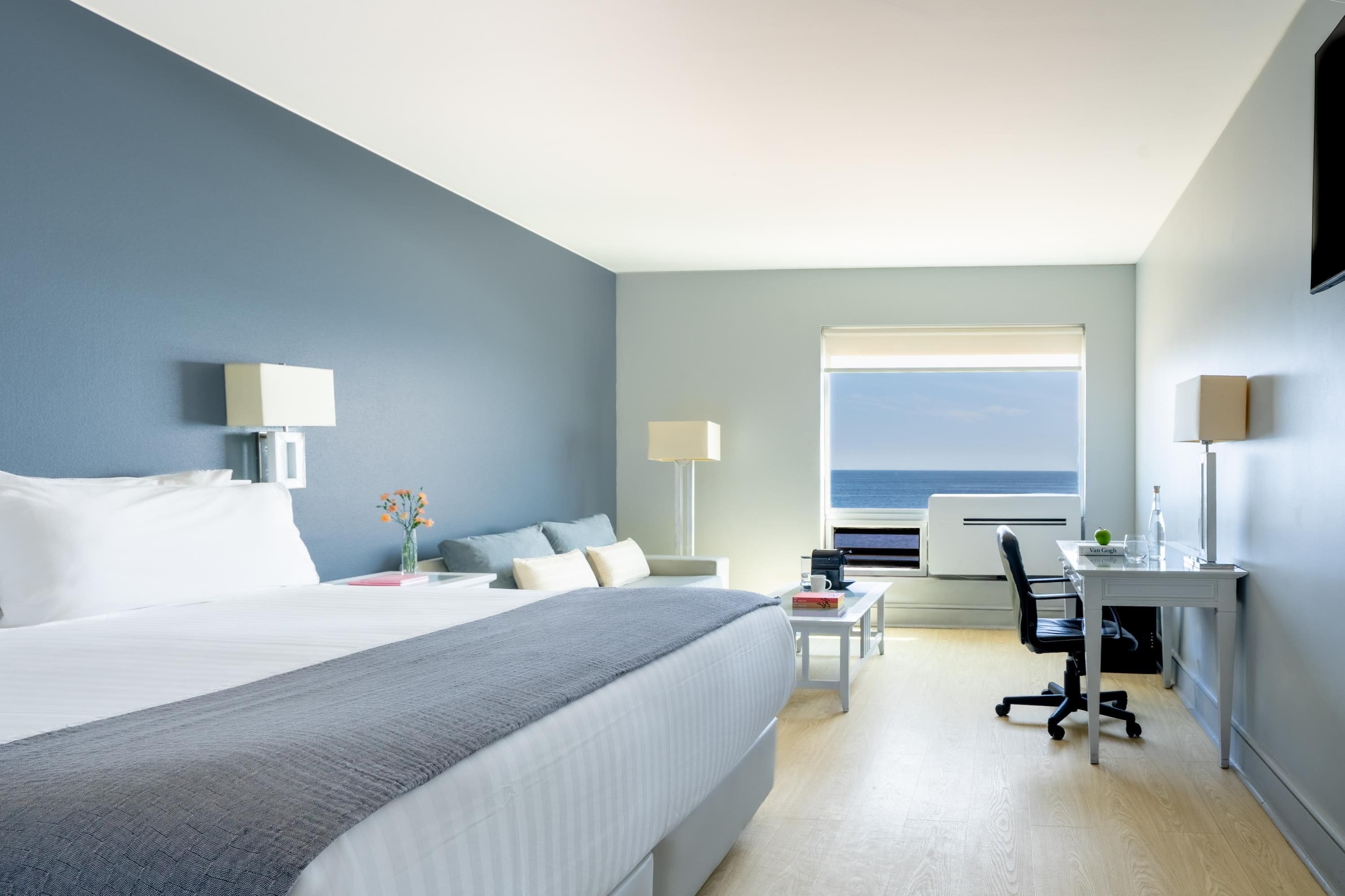 Habitación de hotel con una cama grande, un escritorio, una silla y vista al mar.
