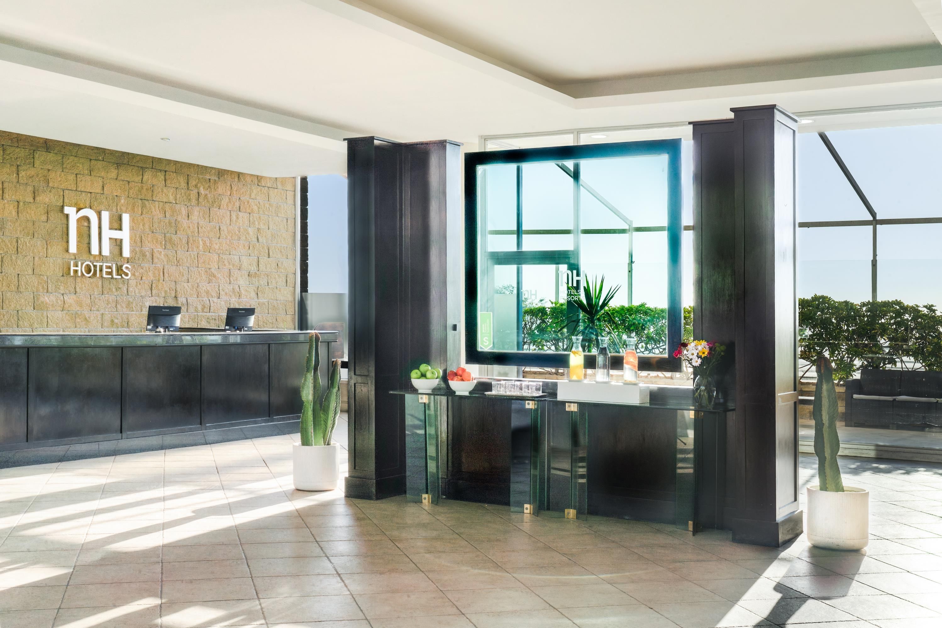 A modern hotel reception area with a stone wall, a reception desk, and a large window offering a view of greenery.
