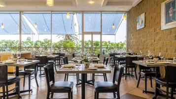 Ein Restaurant mit mehreren Tischen und Stühlen, großen Fenstern und einer Ziegelwand.