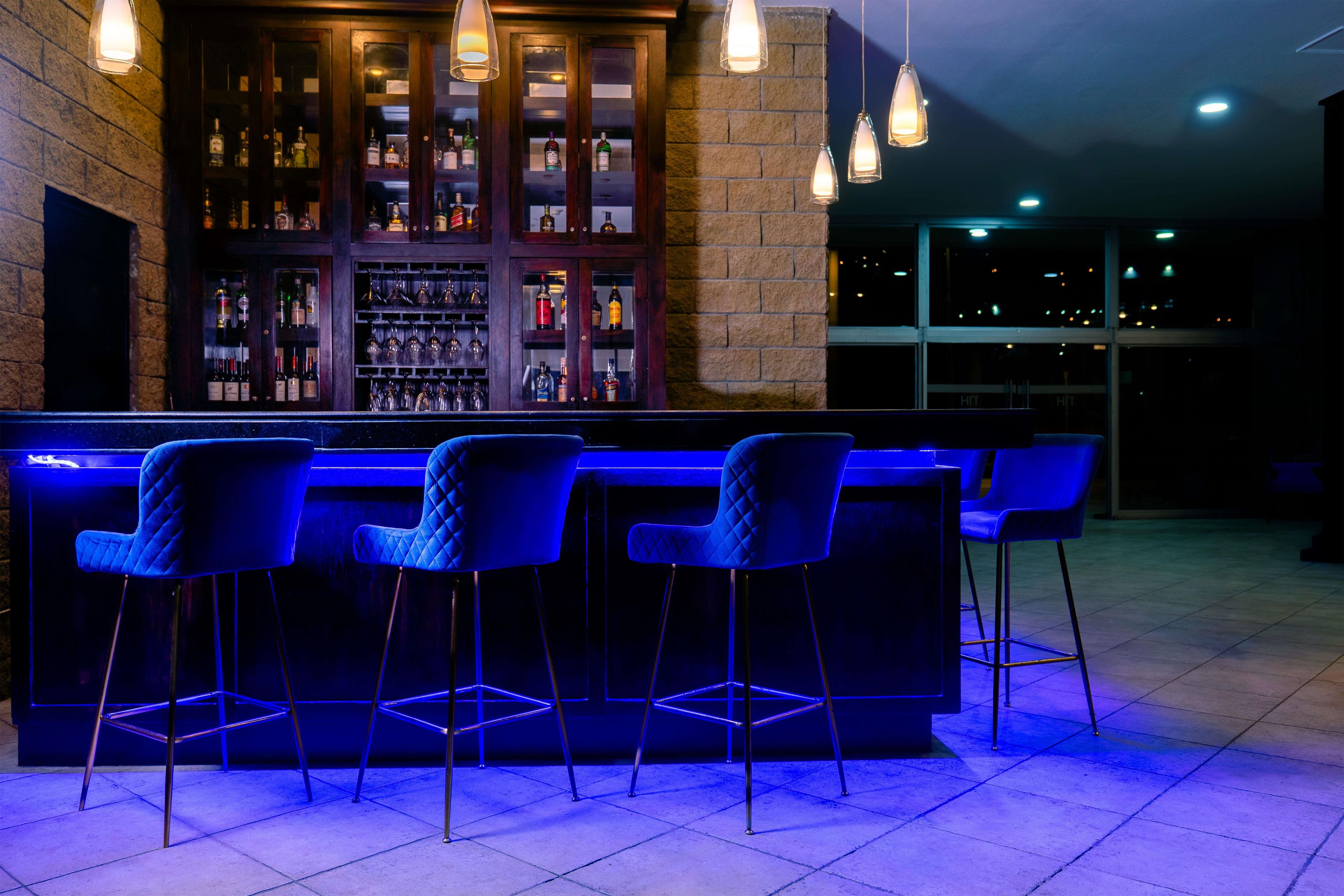 Uma área de bar com balcão e quatro banquetas azuis.