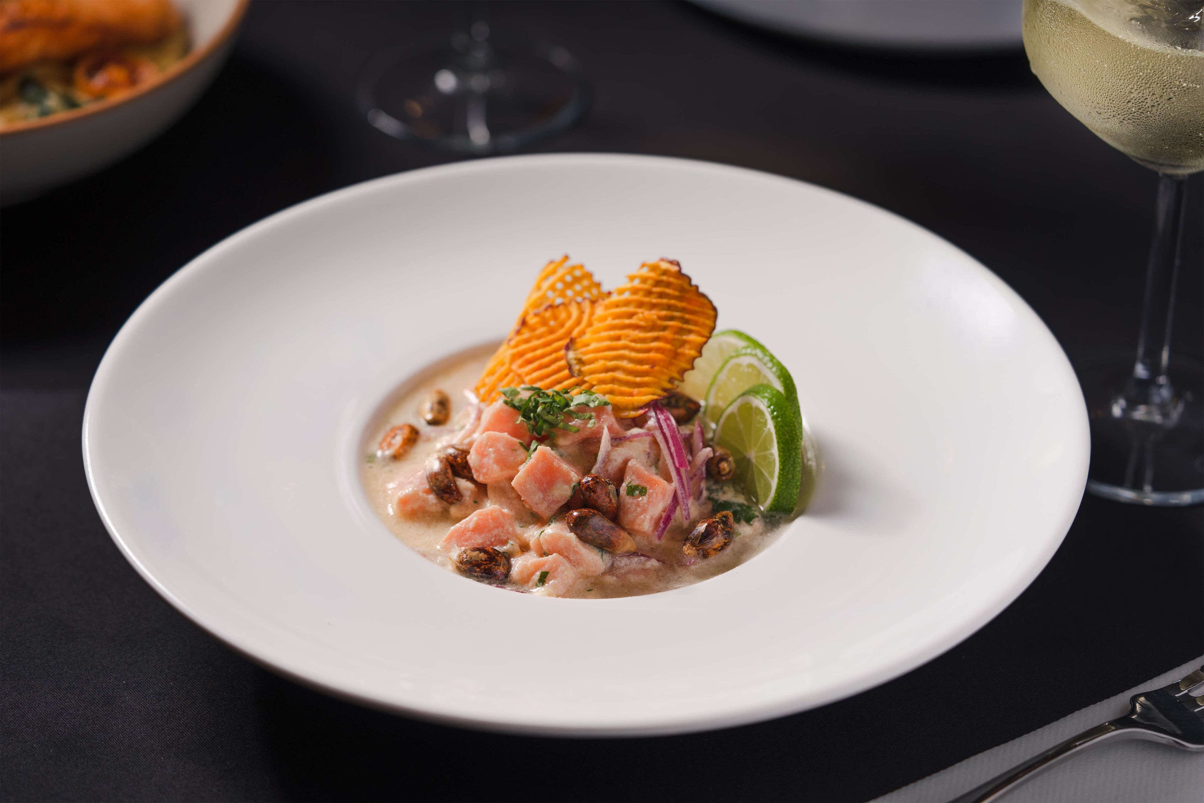 A white plate with a seafood dish, a glass of white wine, and a fork on a dark table.