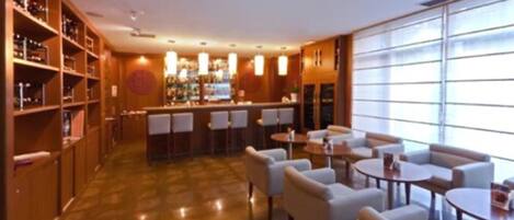 A hotel lobby with a bar area, seating arrangements, and a large window providing natural light.