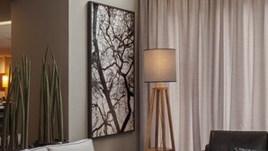Un salon moderne avec un canapé gris, un canapé noir, une lampe sur pied, un tableau représentant un arbre et un tapis à rayures.