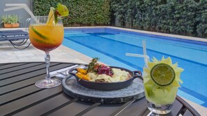 Une table à manger avec un repas et deux boissons, placée au bord d’une piscine.