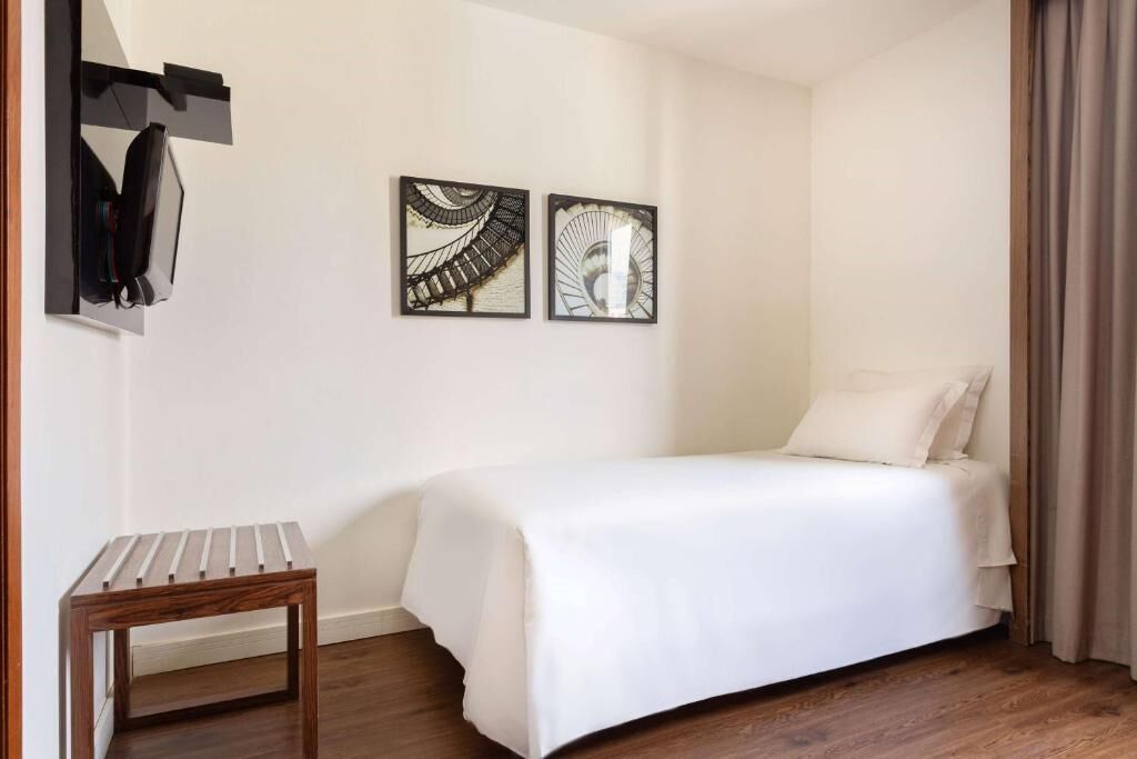 A hotel room with a bed, a small wooden table, and two wall-mounted artworks.