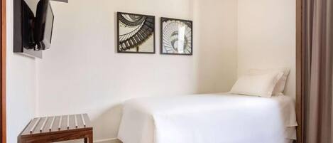 A hotel room with a bed, a small wooden table, and two wall-mounted artworks.