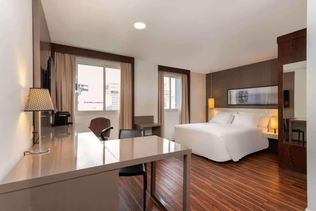 Une chambre d’hôtel avec un lit, un bureau, une chaise, une lampe et un téléviseur.
