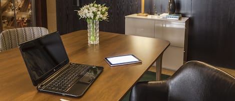 Un salón de conferencias con una computadora portátil, una tableta y un florero sobre una mesa de madera.