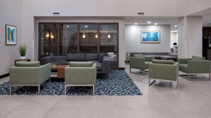 Un lobby moderno con un sofá modular, sillones verdes y una alfombra estampada.