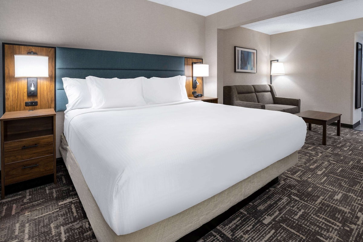 A hotel room with a large bed, two bedside tables with lamps, a chair, and a small table.