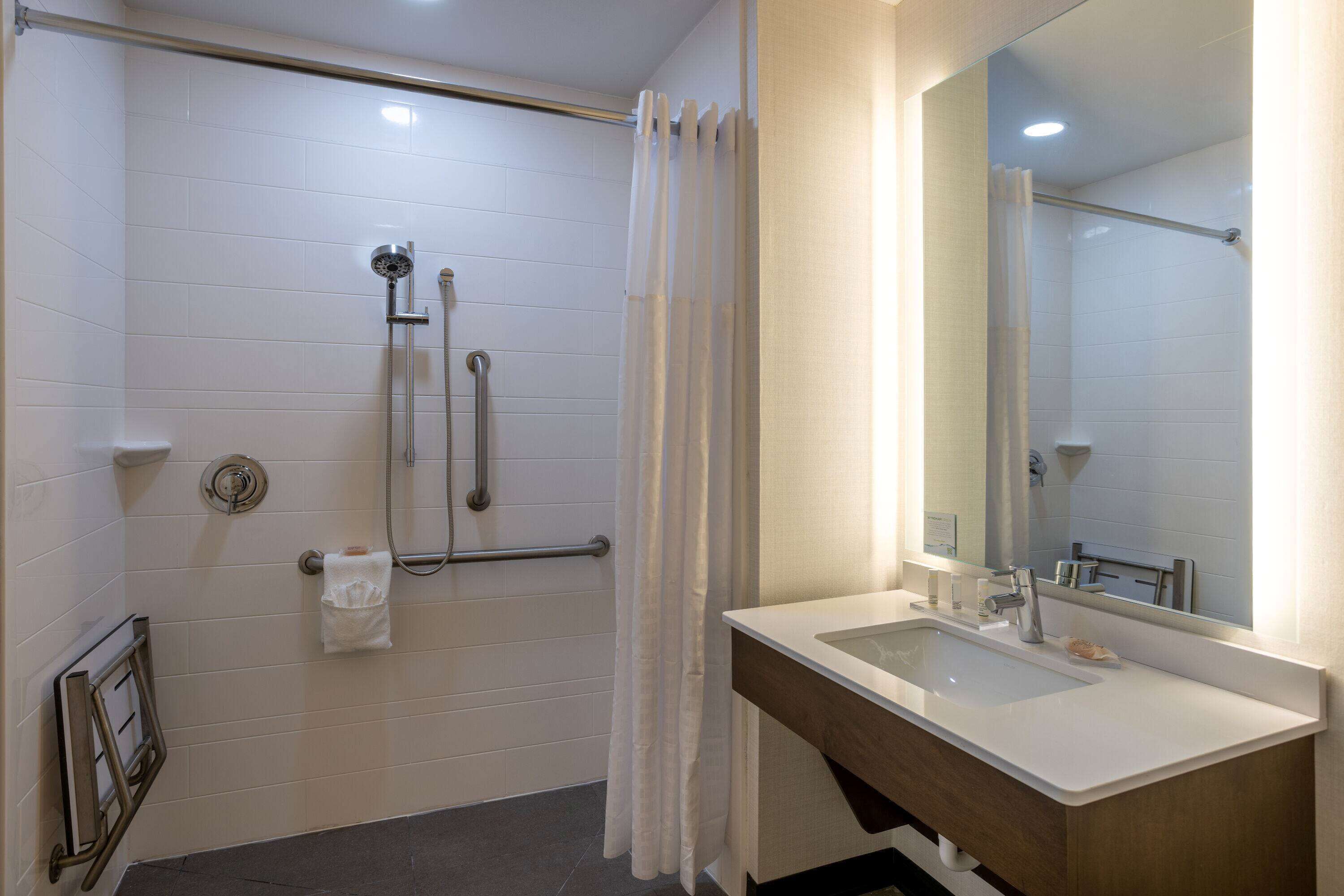 Un baño moderno con cabina de ducha, barras de apoyo, lavamanos y espejo.
