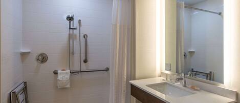 Un baño moderno con cabina de ducha, barras de apoyo, lavamanos y espejo.