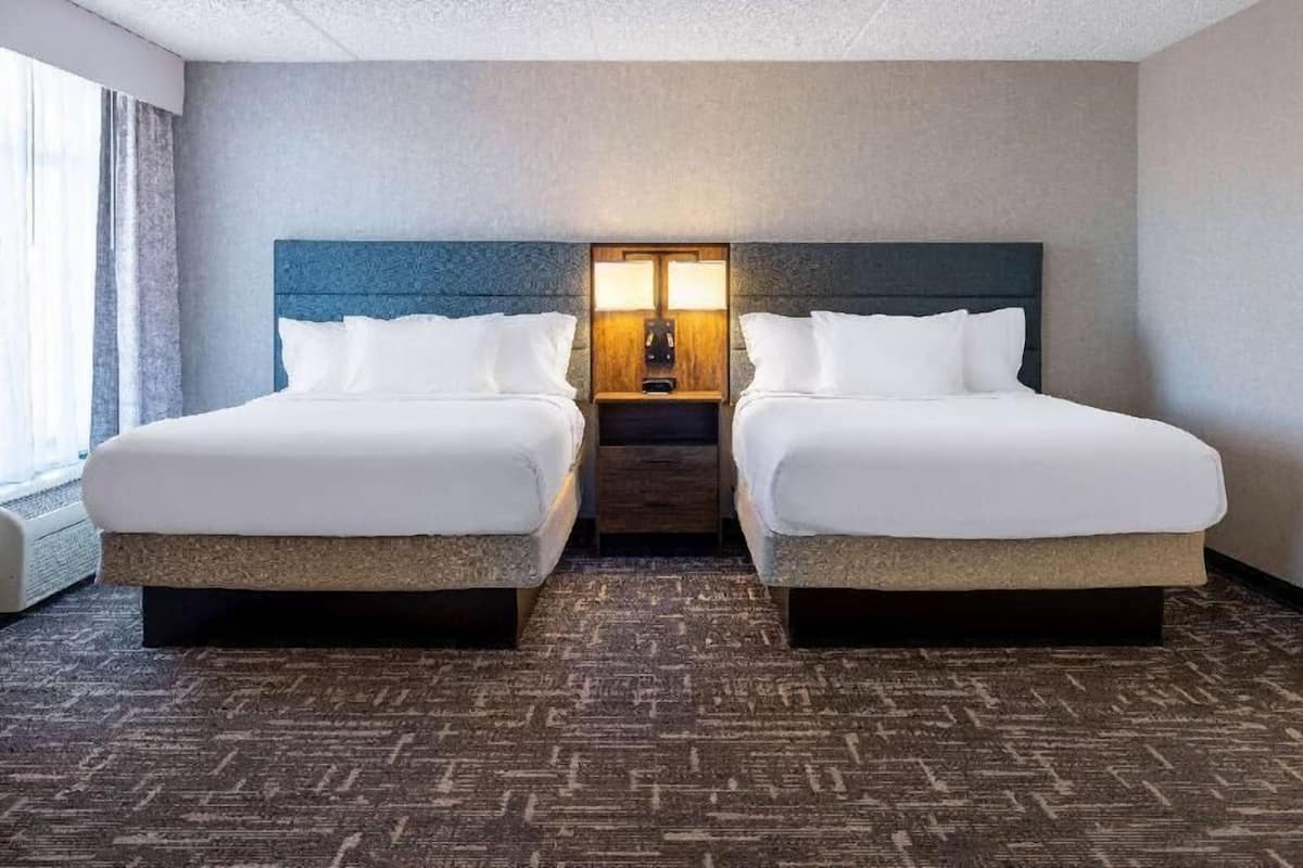 A hotel room with two beds, a nightstand with lamps, and a carpeted floor.