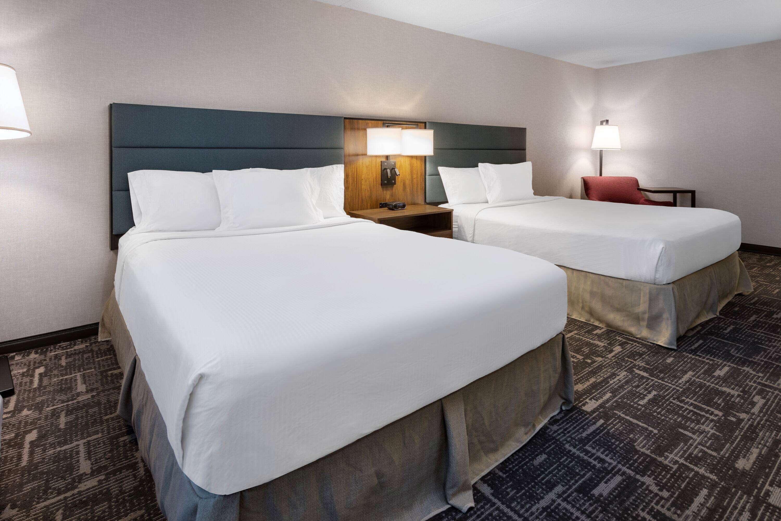 Habitación de hotel con dos camas, una mesita de noche, una lámpara y una silla.