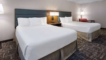 Habitación de hotel con dos camas, una mesita de noche, una lámpara y una silla.