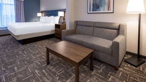 Una habitación de hotel con una cama, un sofá, una mesa de centro y una lámpara.