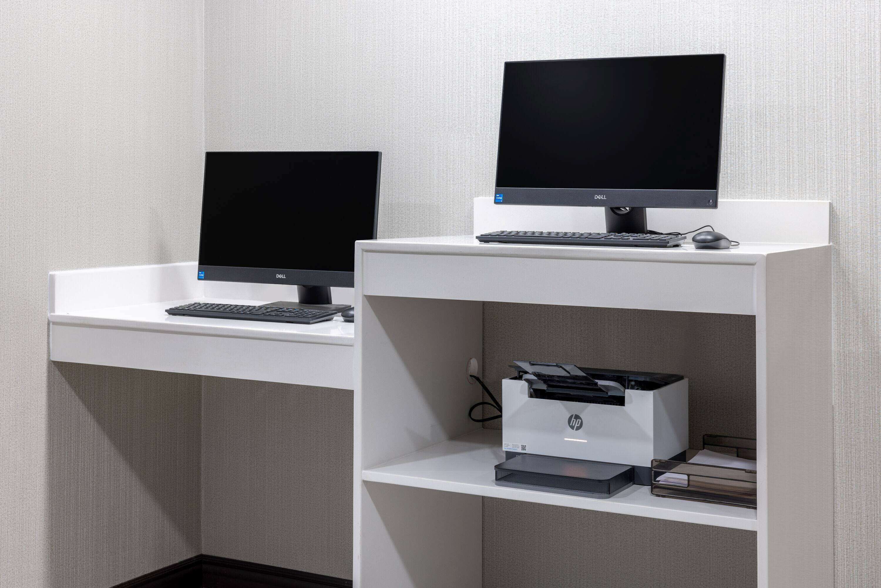 Dos escritorios de computadora con monitores, teclados e impresora.