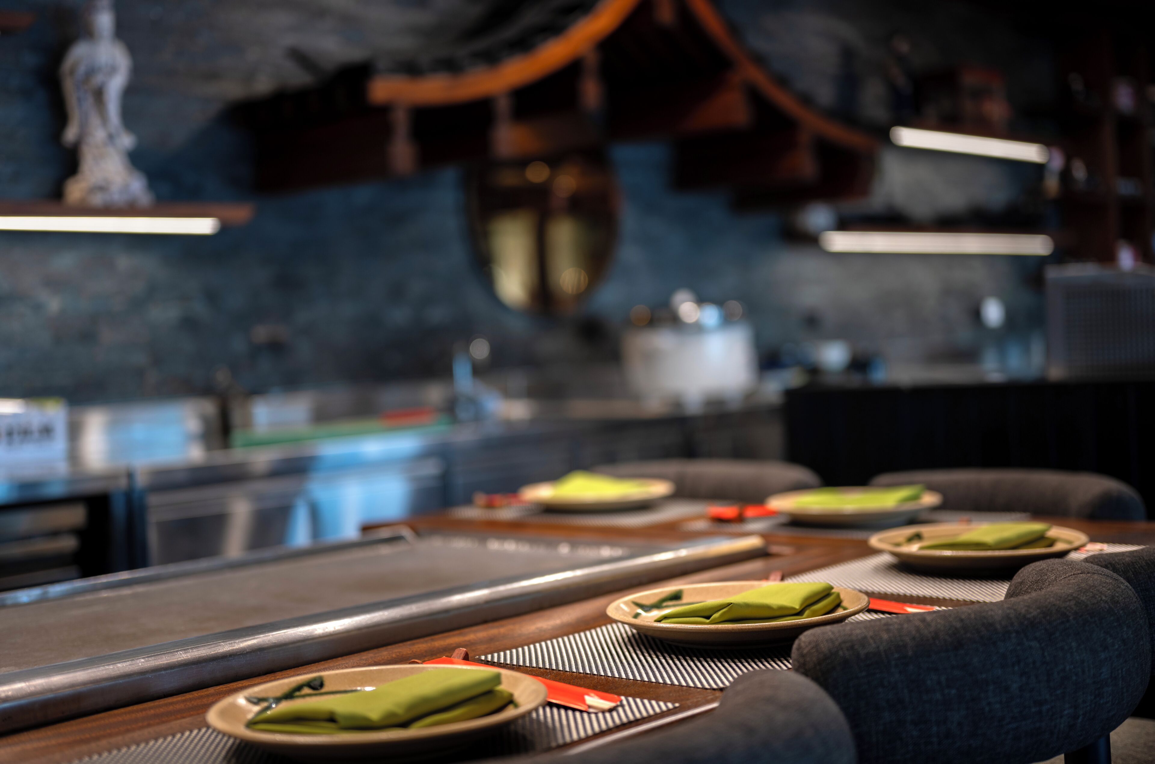 Un restaurante con una larga mesa, platos con servilletas verdes y un interior moderno y oscuro.