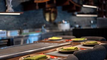 Un restaurante con una larga mesa, platos con servilletas verdes y un interior moderno y oscuro.