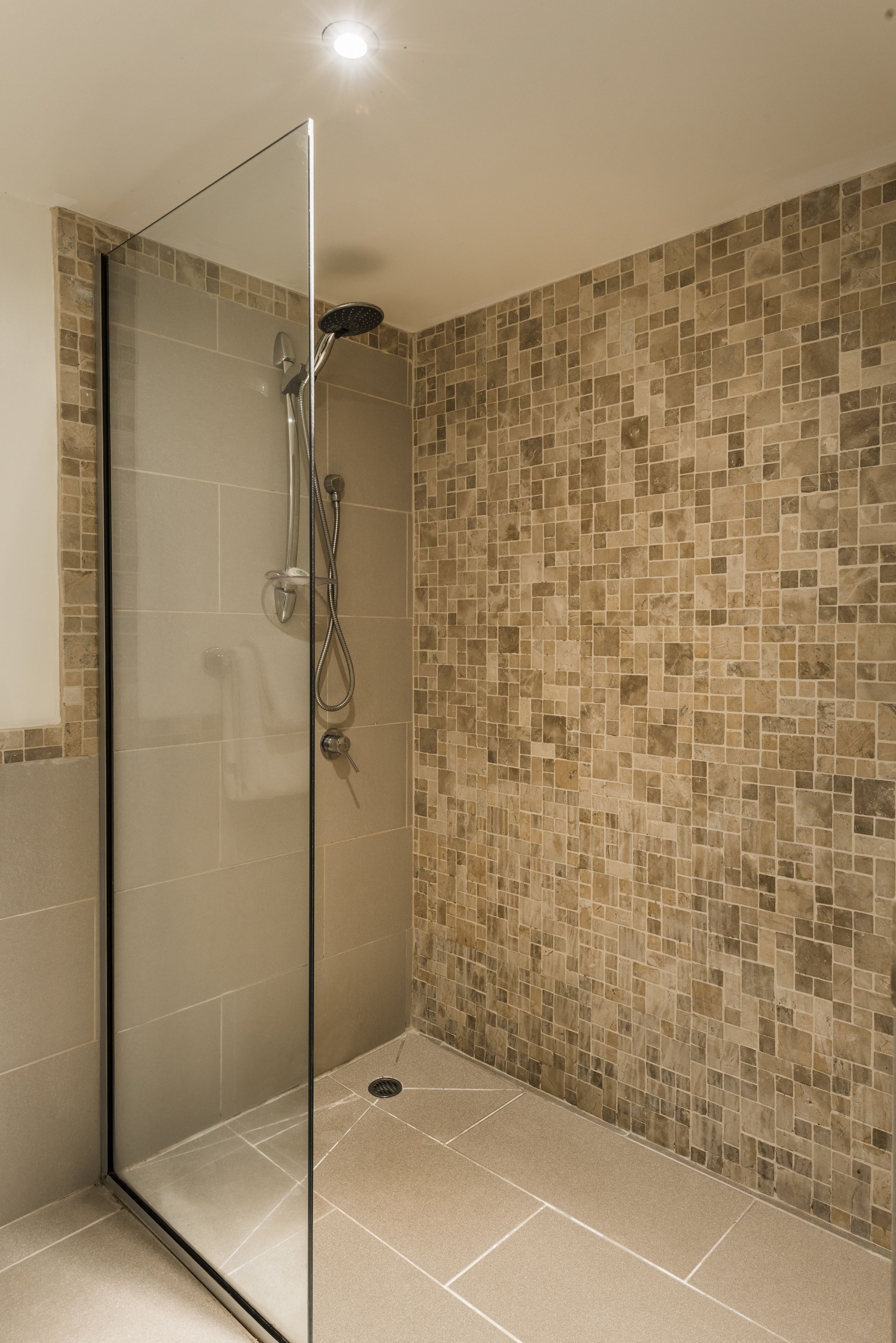 A glass-enclosed shower area with a tiled floor and walls.