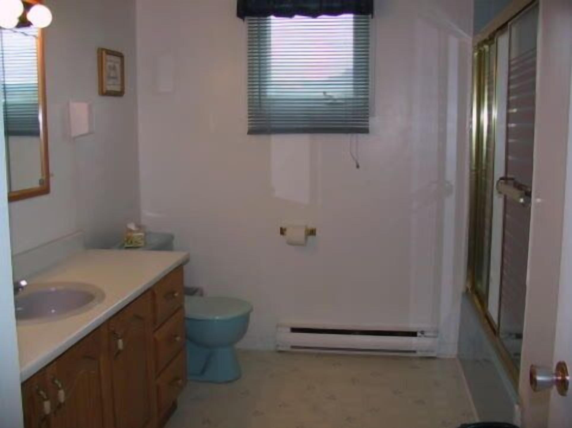 Un baño pequeño con lavamanos, inodoro y ventana con persianas.