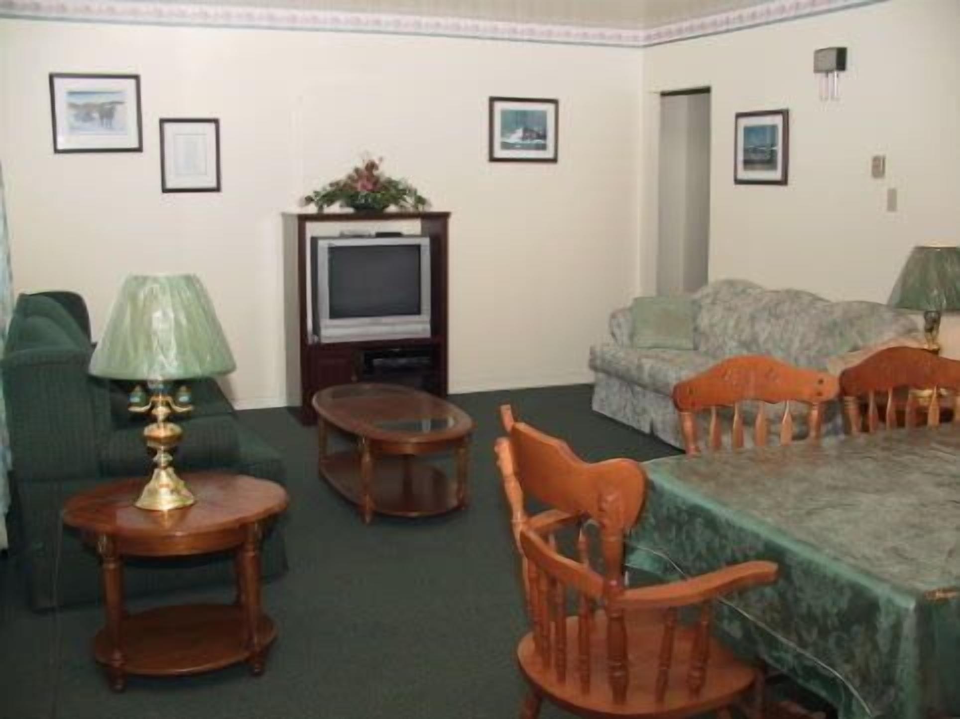 A living room with a green sofa, a wooden coffee table, a television, and a dining table with chairs.