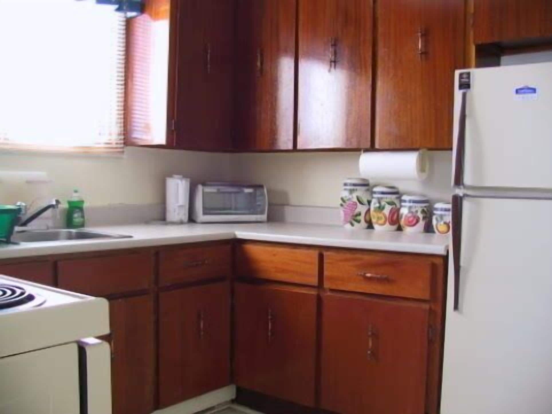 A kitchen with wooden cabinets, a microwave, a refrigerator, and jars on the counter.