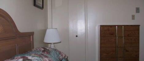 Quarto com cama de madeira, colcha florida, abajur e guarda-roupa.