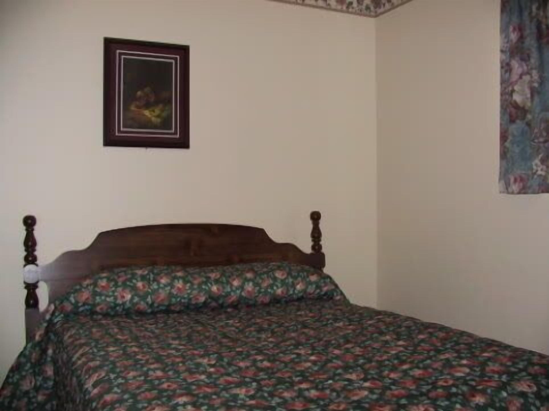 A bedroom with a wooden bed, floral bedding, a framed picture on the wall, and a floral curtain.