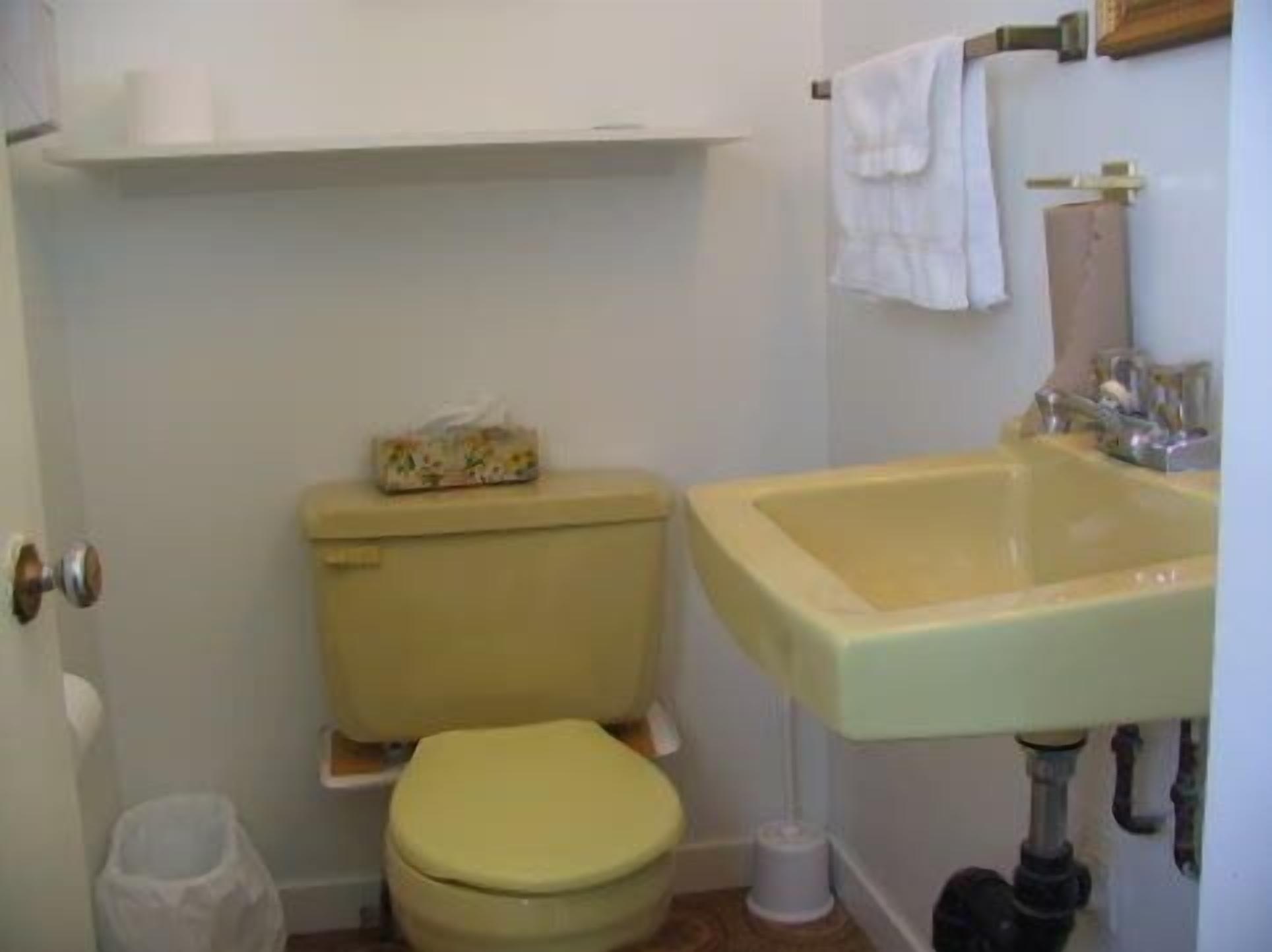 A small bathroom with a toilet, sink, and a shelf above the toilet.