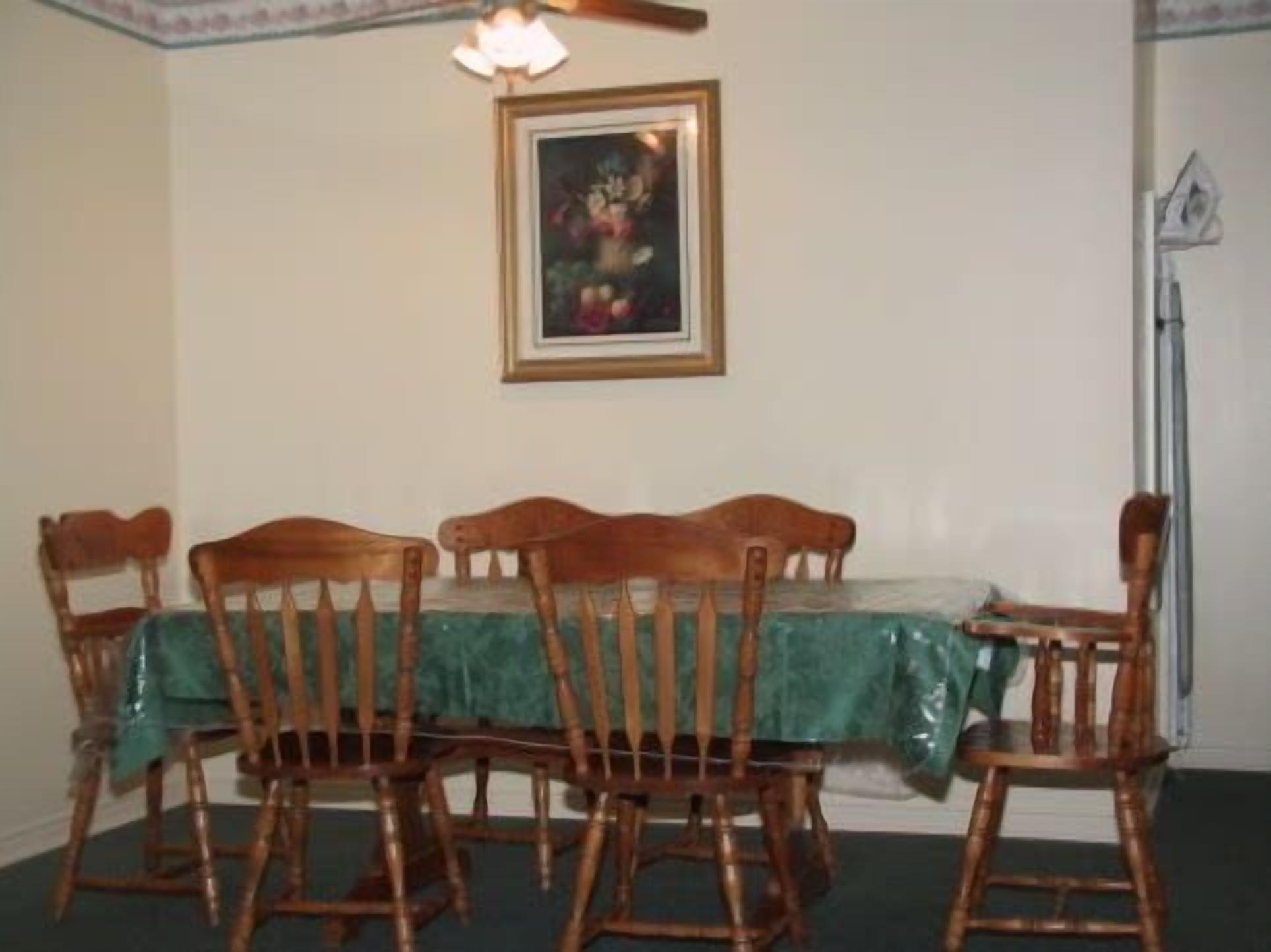Un comedor con mesa y sillas de madera, mantel verde y un cuadro en la pared.